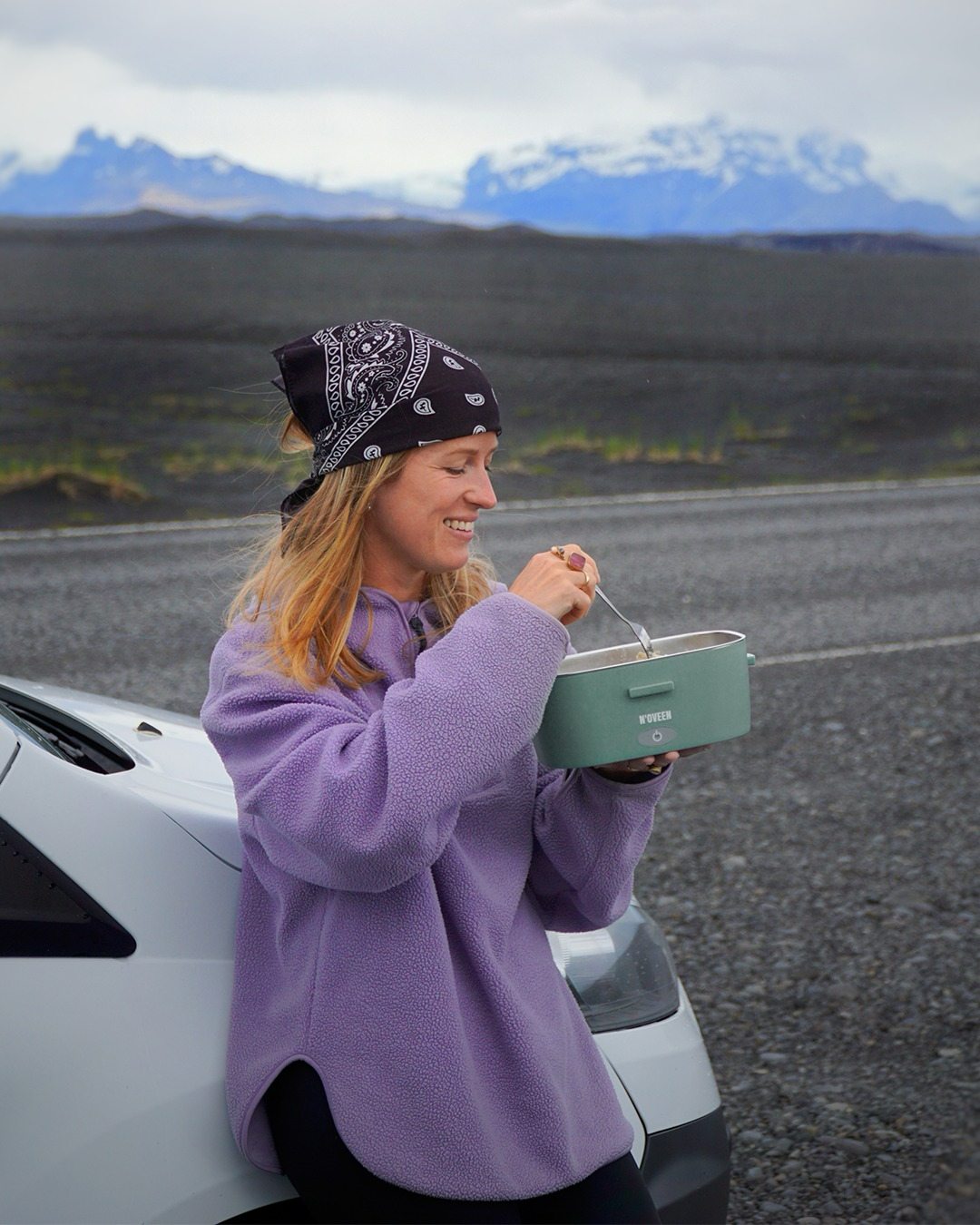 Traveller eating a hot meal from the lunch box next to her car on an Icelandic road